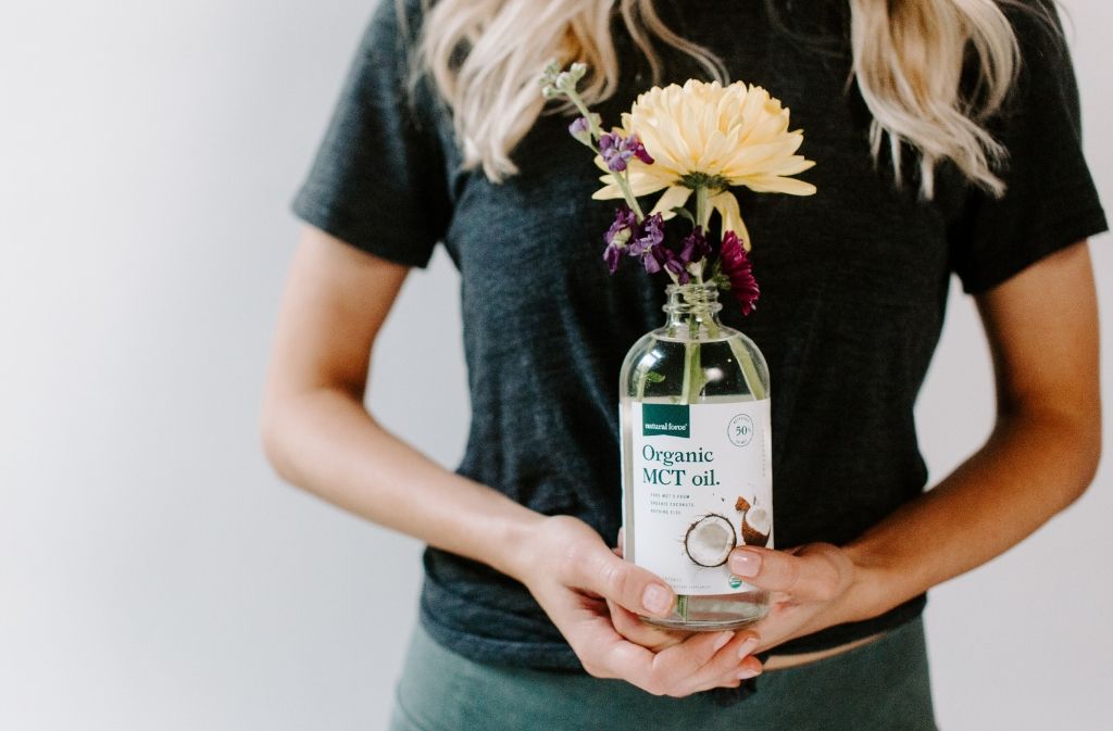 woman cradling a bottle of natural force organic mct oil containing flowers in front of her waist