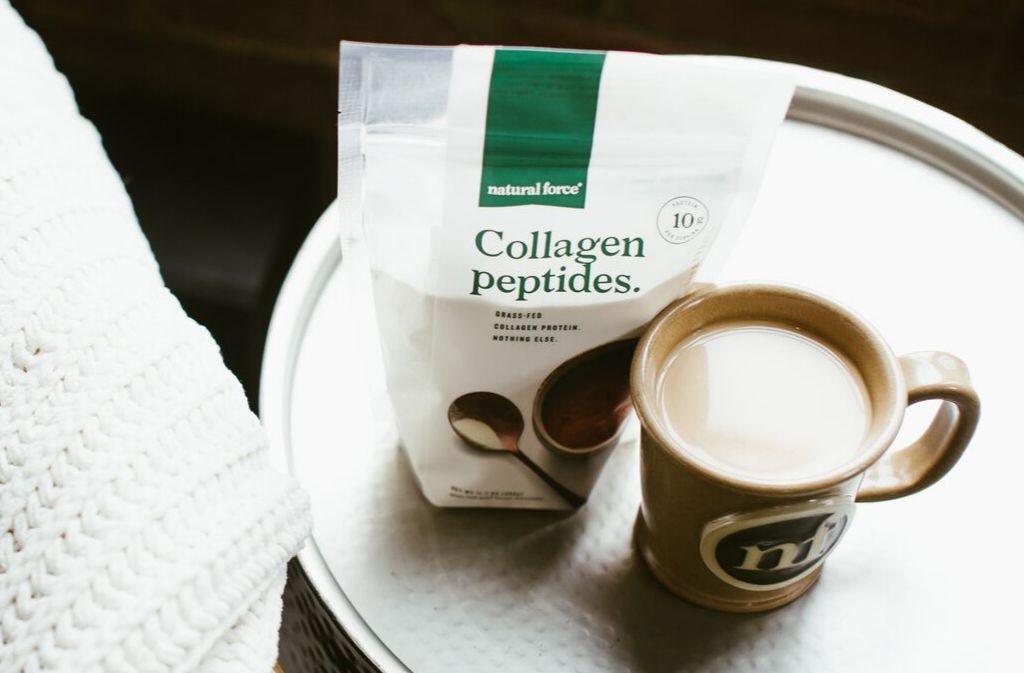 a bag of natural force collagen peptides beside a mug of keto coffee on a metal tray