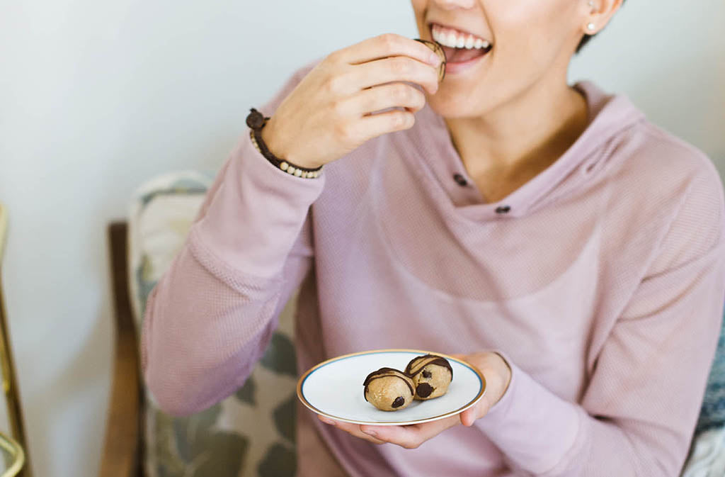 woman smiling while raising a chocolate chip keto cookie dough bite to her mouth
