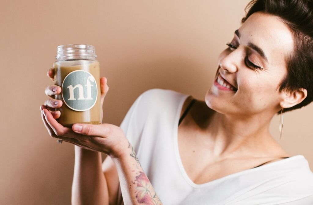 woman smiling and holding up a glass of low carb salted caramel cold brew