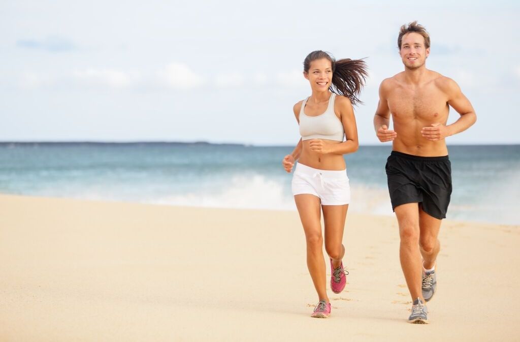 man and woman staying in shape while traveling by jogging on the beach 