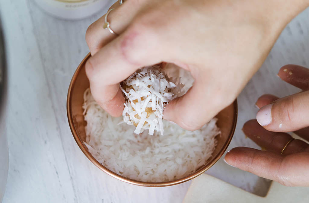 hand dipping low carb energy balls into a bowl of shredded coconut