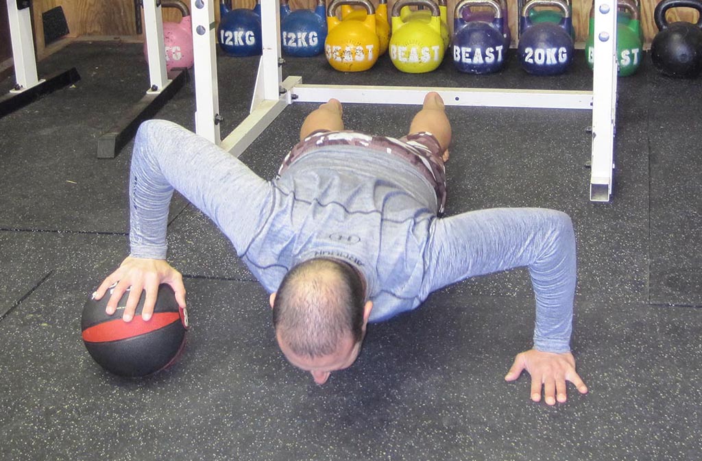 man doing a one-armed medicine ball push up