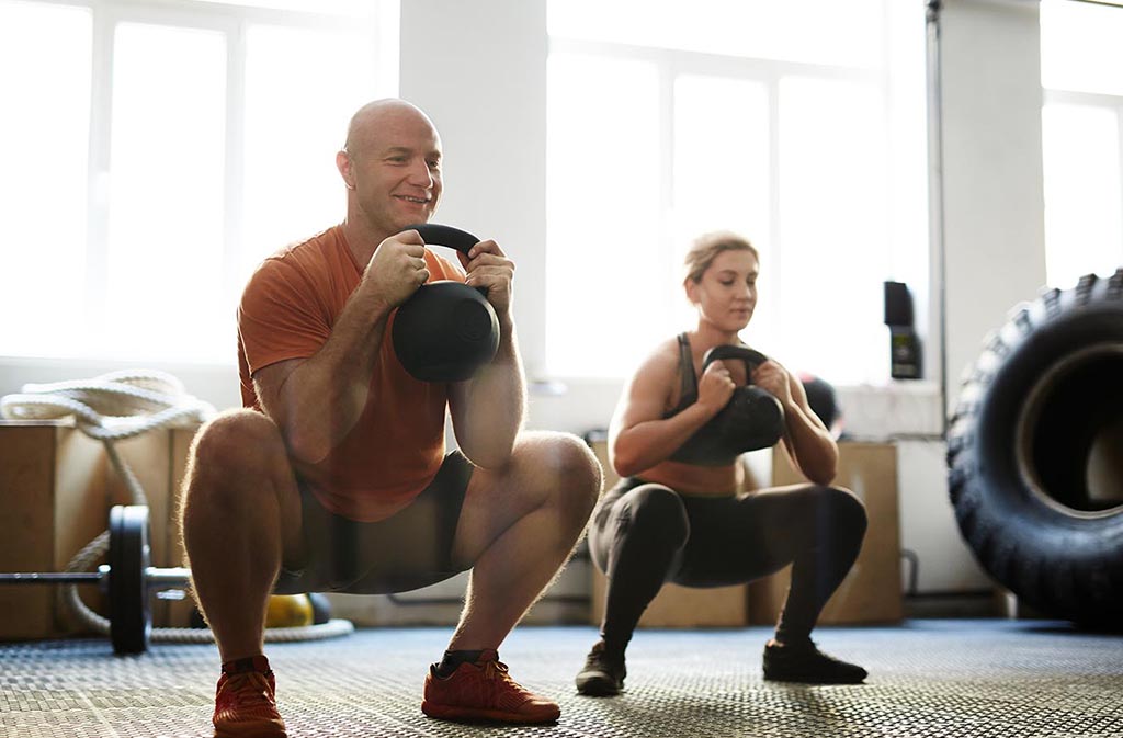 man and woman squatting while holding kettlebells