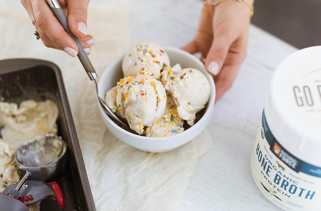 bowl of dairy free cake batter nice cream with sprinkles beside natural force organic bone broth protein