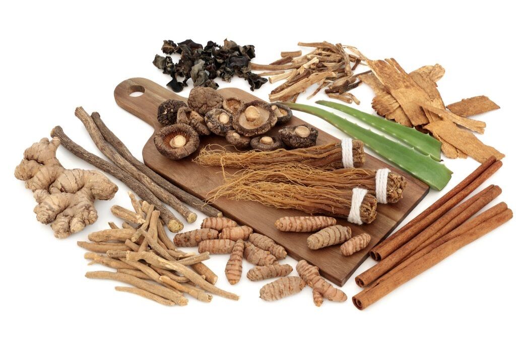 a variety of adaptogenic herbs and spices displayed on a cutting board on a white surface