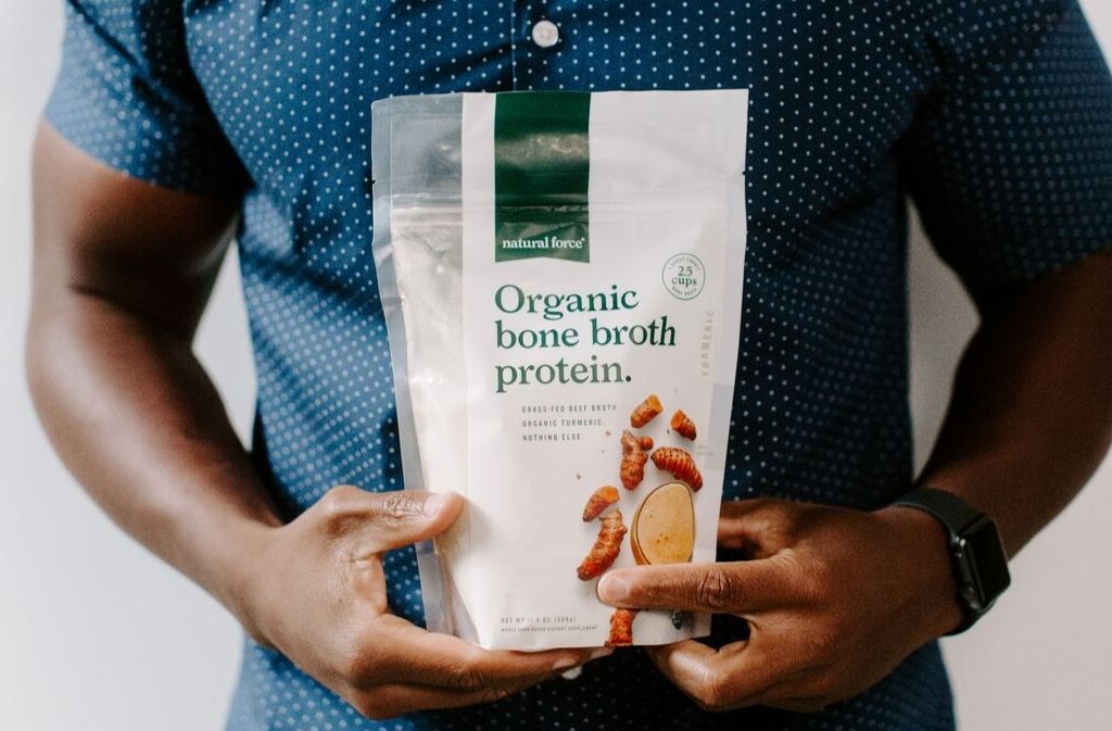 fit man in a blue shirt holding a bag of natural force organic bone broth protein