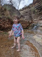 Infant standing in water outdoors.