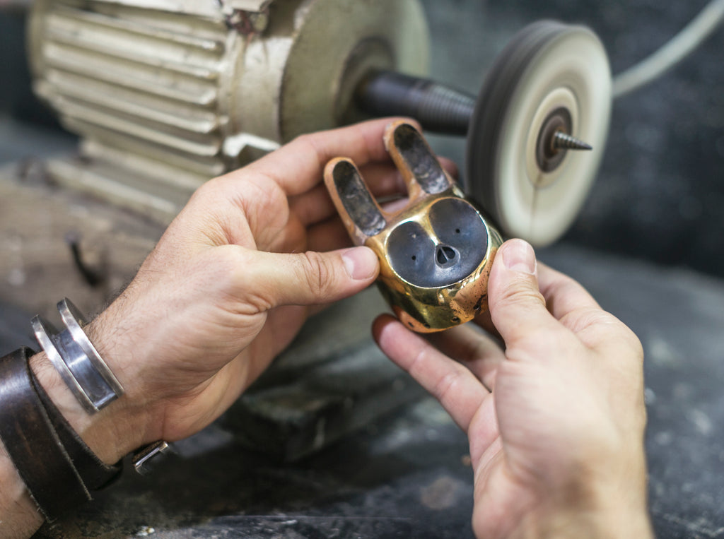 A close up image of a hands holding a brass creature head and buffing it on a buffing wheel 