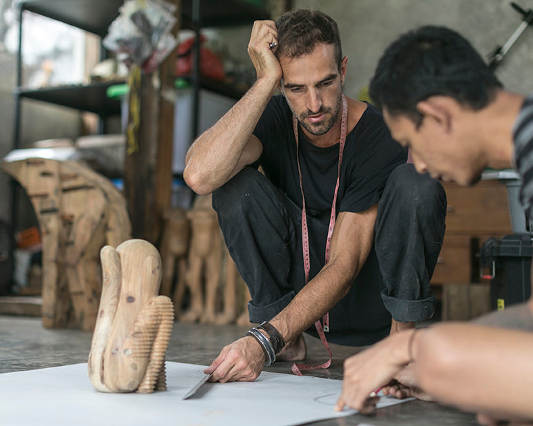 Two men sitting on the floor over a pattern and a wooden sculpture designing