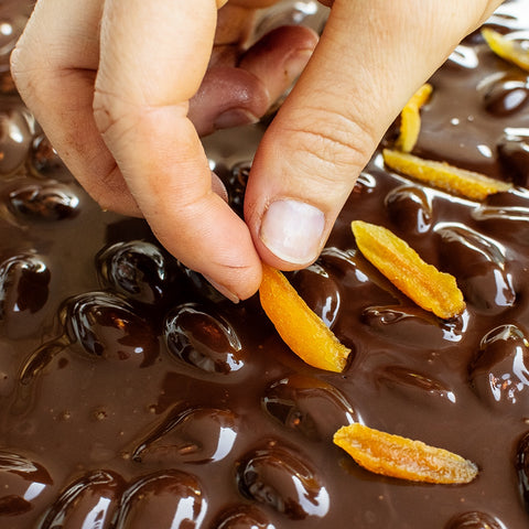 Hand dipping an apricot in a Dark chocolate bark with almonds