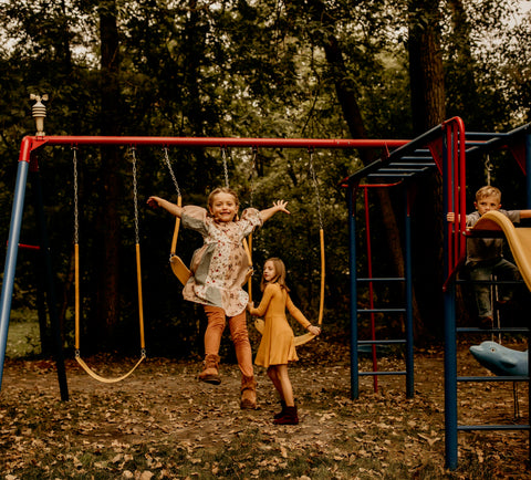 Two kids playing on a swing set, laughing.