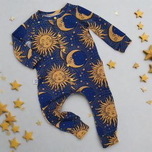 Flay lay image of a handmade baby romper made with dark blue fabric featuring a 90s inspired sun and moon print in gold