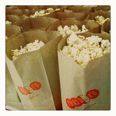 Curio & Co. thinks about popcorn at the movies. Photo of Popcorn in Curio & Co. brown paper bags with logo. Curio and Co. www.curioandco.com
