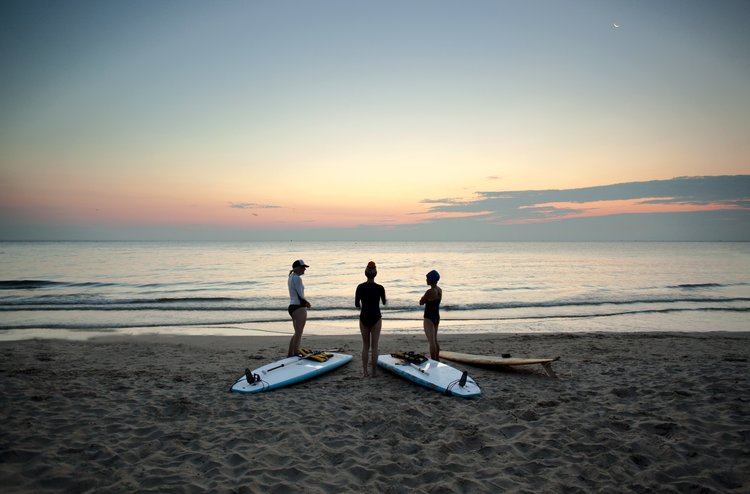 three women with surfboards on the beach sunrise