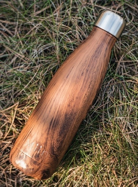 Genanvendelig drikkedunk i Teaktræ design fra Miin Bottle ligger ned på græs