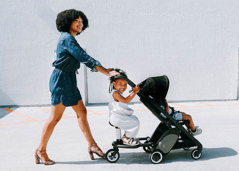 Woman pushing child in Bugaboo Ant stroller with a second child sitting on the ride along board attachment