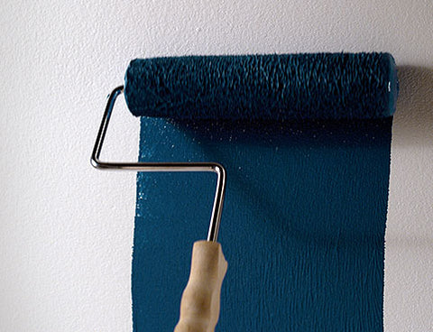 A paint roller painting dark blue on a white wall.
