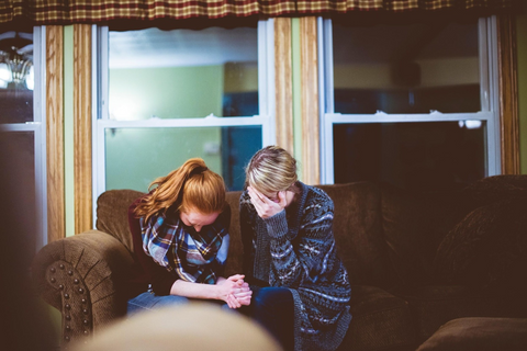 Two women crying and holding hands and comforting each other as the grieve.