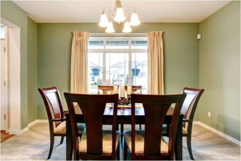 A dining room with walls painted light green, beige curtains, a bright chandelier and a dark brown dining room table with chairs.