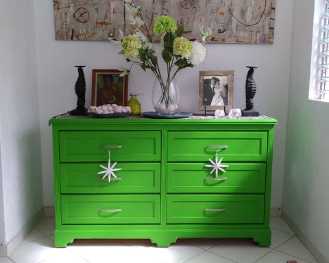 A bedroom dresser that has been painted a bright green with starfish decorations hanging from the drawer handles, paint colours to brighten up your space.