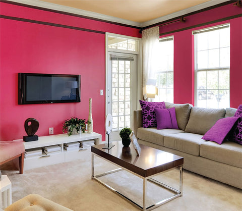 A living room with bright pink painted walls, beige couch and purple pillows, paint colours to brighten up your space.