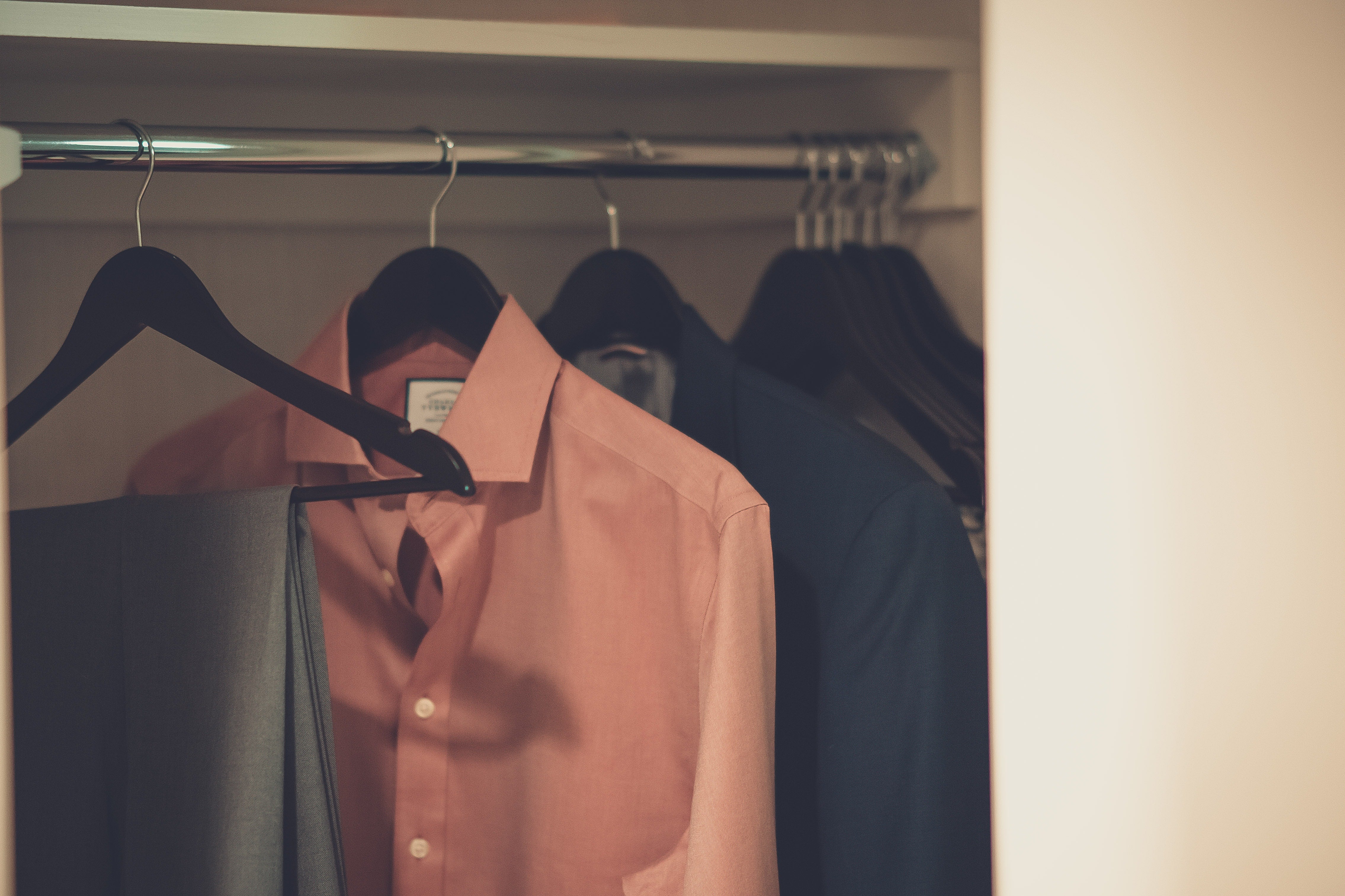 Stylish, gray men’s trousers and two shirts hung on black wooden hangers.