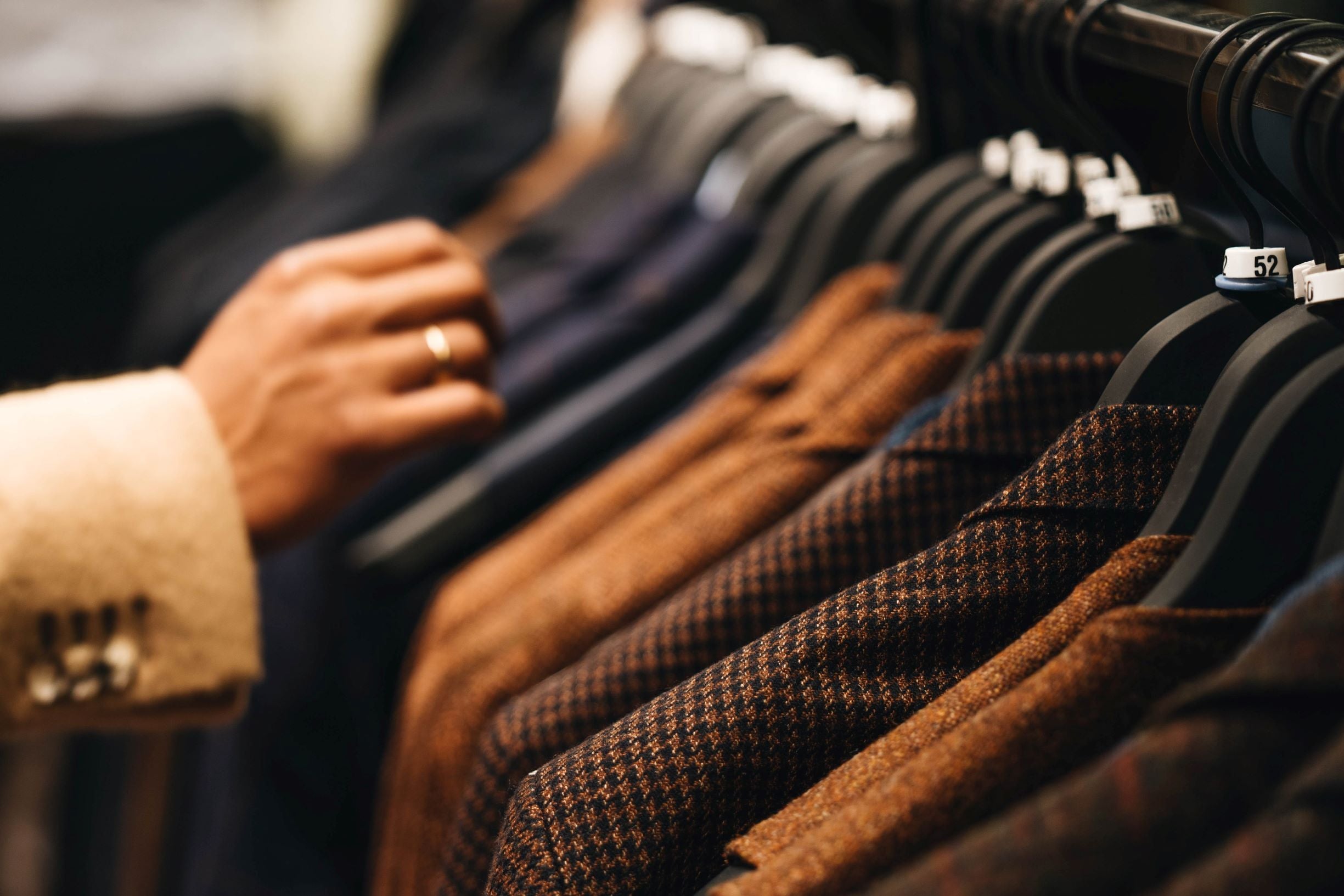 A man in a jacket looking at the men’s patterned blazers lined up on black, elegant hangers in a store