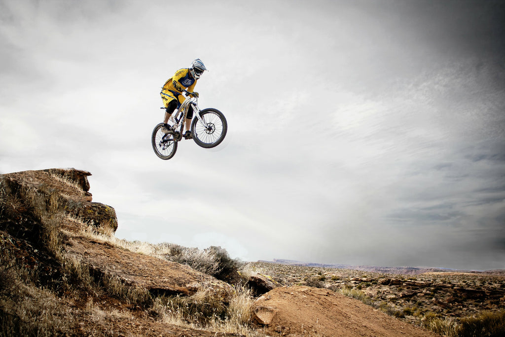 man jumping from a cliff on a mountain bike trail