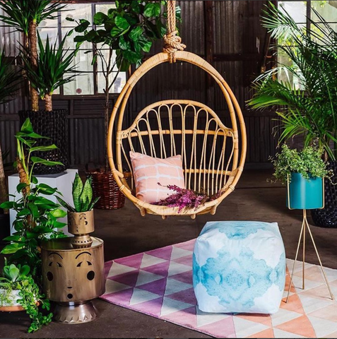 hanging rattan swing above pink triangle rug. Boho room with palms. 