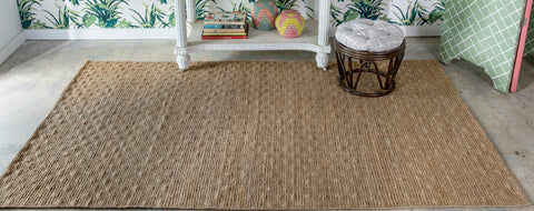 natural jute area rug infront of a palm tree wall papered wall.