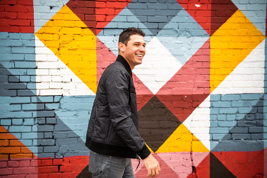 Warstic co-owner Ian Kinsler wearing the Warstic x Billy Reid Icon Player's Jacket, in front of a multi-colored mural.
