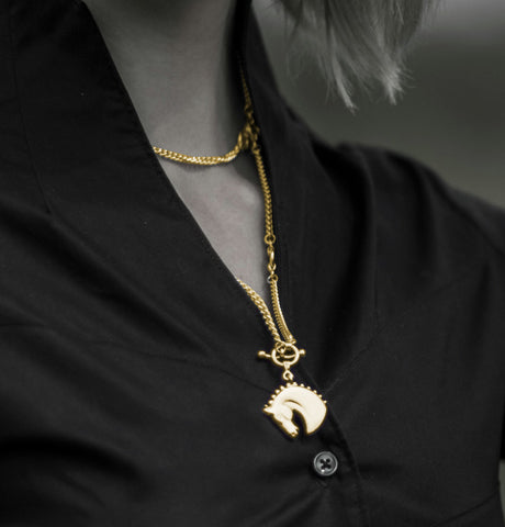 Model wearing a solid 9ct gold Farah horsehead necklace on model next to horse
