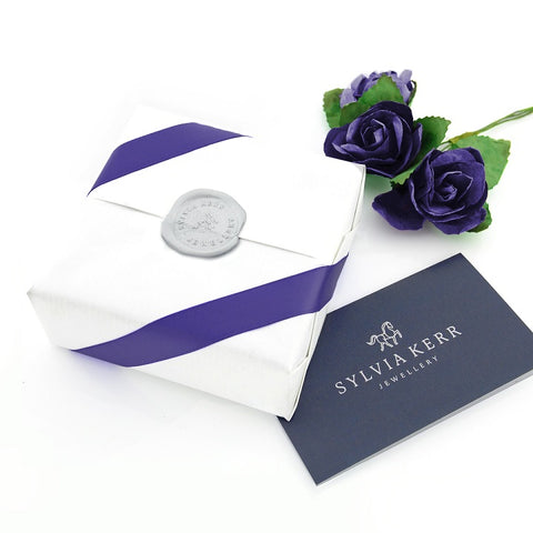 Giftwrapped parcel with crisp white pinstripe wrapping paper with luxury purple ribbon and wax seal