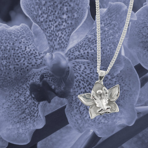 solid silver carved orchid necklace in front of purple image of orchid