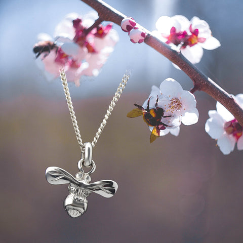 Solid silver honey bee necklace next to apple blossum
