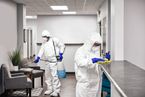 two people dressed in protective clothing disinfecting an office space to help prevent the spread of COVID-19