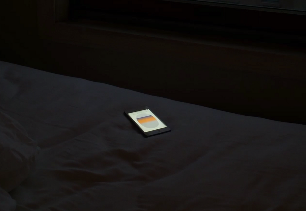 A bright iPhone with the flight simulator app open sits face-up on a bed in a dark room.