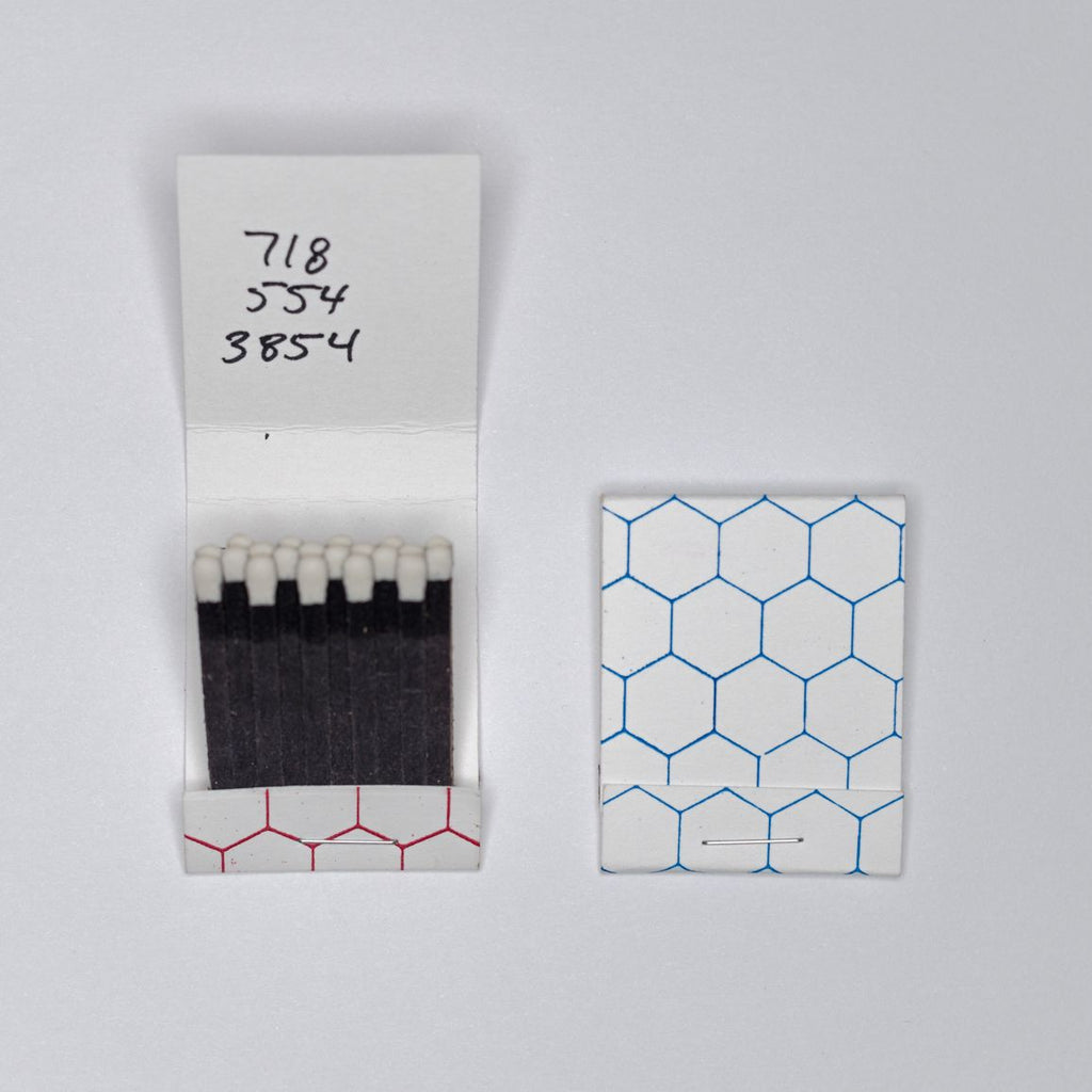 An open matchbook lays flat next to a closed one on a white surface. The open one reads "718-554-3854" on the top, written in black marker.