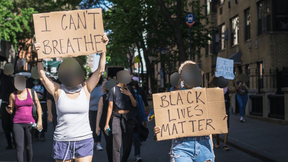 Black Lives Matter protest in the street with signs as dark ovals blur their faces.