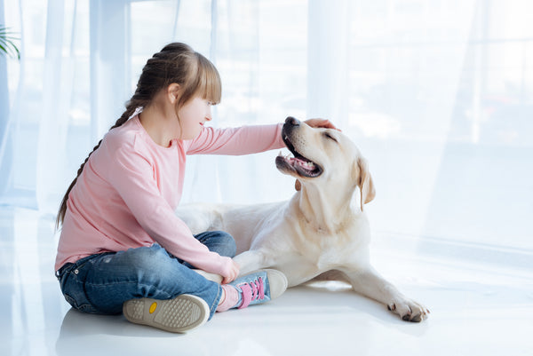 young girl in pink shirt sitting on floor petting her yellow labrador retriever