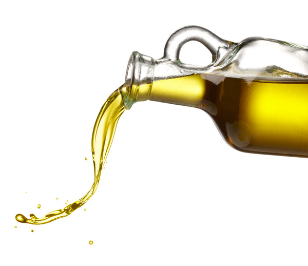 Organic Extra Virgin Olive Oil being poured from a clear glass bottle
