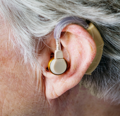 Photo of a hearing aid being worn in the ear of an old woman