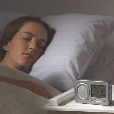 Woman asleep in bed with a Sound Oasis Travel Sound Therapy System on the bedside table