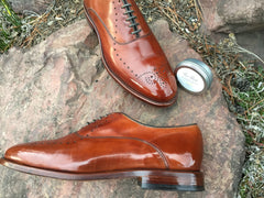 Pair of Mirror Shined Allen Edmonds Walnut Weybridge on a rock, with High Shine Paste reflecting in the toe