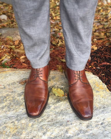 Men's Style Shot – Front shot of Brown Magnanni Derbies and Grey Agave Denim Slacks, Fall Leaves in the Background, Standing on a Flagstone