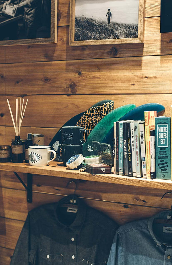 A shelf displaying assorted books and accessories, above to hanging TS shirts.