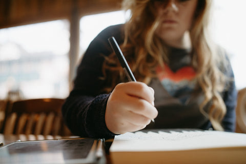 Shelby Campbell sitting in Leavenworth coffee shop wearing a grey graphic t-shirt with a heart and mountain scene illustration. PNW Style. Pacific Northwest. Drawing. Sipping Coffee. Cafe.  Leavenworth, Washington. Mountains. Mountain Style.