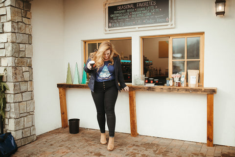 Women wearing a blue graphic t-shirt with a triangle shaped mountain illustration on the front. Black denim jeans. High Waisted. Booties. Coffee. Outdoor Coffee Shop in Leavenworth, Washington. PNW Style. Pacific Northwest.