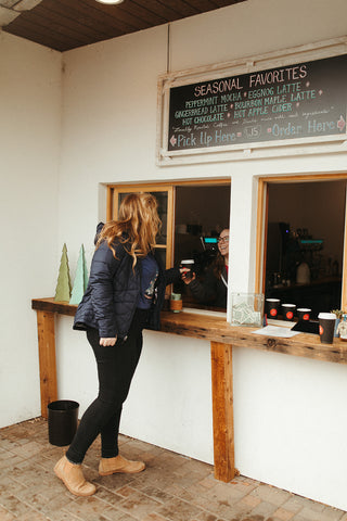 Women wearing a blue graphic t-shirt with a triangle shaped mountain illustration on the front. Black denim jeans. High Waisted. Booties. Coffee. Outdoor Coffee Shop in Leavenworth, Washington. PNW Style. Pacific Northwest.